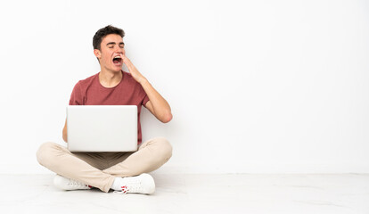 Teenager man sitting on the flor with his laptop yawning and covering wide open mouth with hand