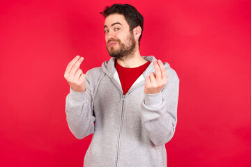 Young caucasian man wearing tracksuit over red background doing money gesture with hands, asking for salary payment, millionaire business