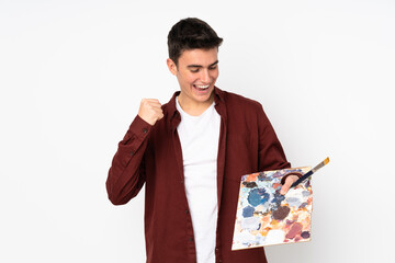 Wall Mural - Teenager artist man holding a palette isolated on white background celebrating a victory