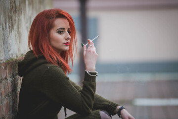 Poster - Red-haired young female in a beautiful winter dress smoking in front of a brick wall