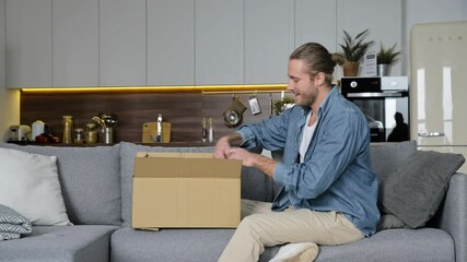 Wall Mural - Smiling attractive man unpacked his parcel, happy about getting a long expected order. Caucasian modern guy shopping in internet stores, buying new clothes online, is review it