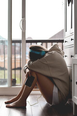 Young teenage girl in headphones sitting on a kitchen floor sad or upset with her head down on her knees