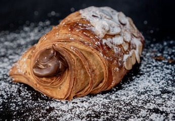 Delicious French style almond chocolatin filled with chocolate on a black table decorated with sugar.