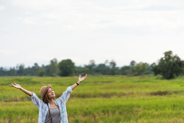 A tourist woman enjoy taking photo of landscape during her summer vacation holiday in the greenery field. A stylish traveler woman in hat taking photo of herself and landscape while relaxing