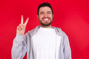 Sticker - young handsome caucasian man in sports clothes against red wall showing and pointing up with fingers number two while smiling confident and happy.