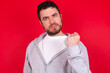 © Jihan - young handsome caucasian man in sports clothes against red background shows fist has annoyed face expression going to revenge or threaten someone makes serious look. I will show you who is boss