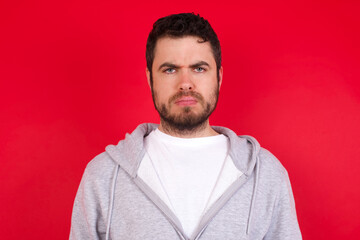 Wall Mural - young handsome caucasian man in sports clothes against red background Pointing down with fingers showing advertisement, surprised face and open mouth