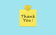 Yellow sticky thank you note and heart isolated on blue background.