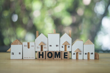 Wall Mural - Wooden block with the word HOME and difference size of small wooden houses model on wood table.