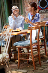 Wall Mural - An older woman have a phone call while spending a time with her young female friend in the bar. Leisure, bar, friendship, outdoor