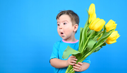 Wall Mural - Fun child with bouquet of tulips, surprised boy against a blue wall.