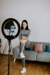 © shevtsovy - Virtual online fitness. Woman virtual workout at home living room. Fitness stretching exercises online women at home with smartphone. Attractive Woman personal trainer coach recording on camera new