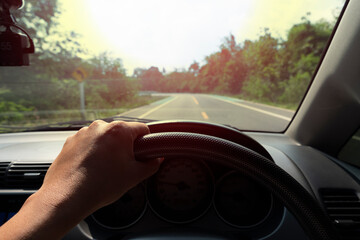 The steering wheel of a car with the driver's hand on one side. On the road to nature With bike lenses beside. Road trip at At Ang Kep Nam Dok Krai Rayong Thailand.