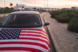 Soft focus of a car parked on the side of the road with the American flag draped on its hood