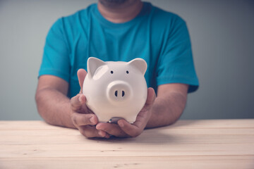 Man holding white piggy bank on wood table in studio room. Concept Business, finance, investment, saving money wealth and financial.