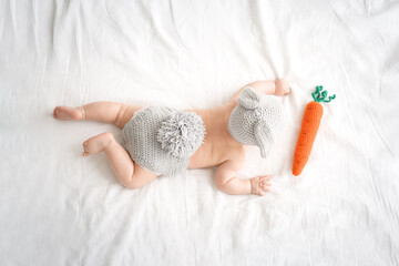 Happy child with bunny ears and lying on a bed with a carrot. Top view                           