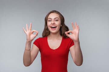 Image of happy young brunette woman isolated over gray background showing OK gesture with both hands