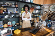 © sofiko14 - Portrait of likable afro american woman in uniform and eyeglasses smiling and looking at camera. Modern shop with various decor on shelves.