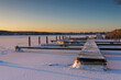 Snow-covered winter landscape with a frozen lake and boat dock at sunset