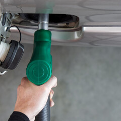 Wall Mural - Gas station worker filling up bronze pickup truck tank (Top View). Closeup hand holding green gas pump nozzle.