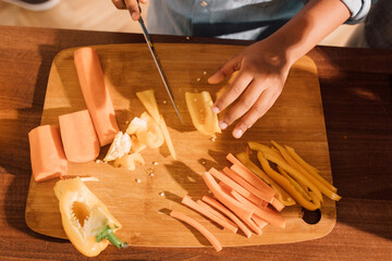 Boy chopping pepper and carrot on wooden chopping board in modern kitchen