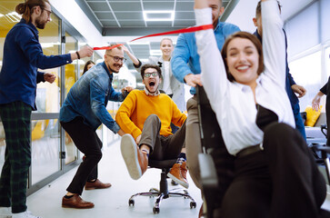 friendly work team ride chairs in office room cheerfully excited diverse employees laugh while enjoy