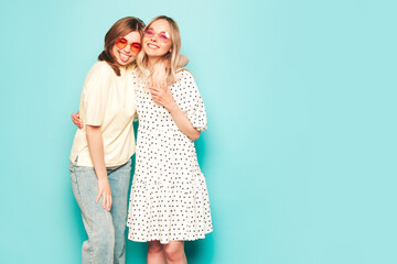 Wall Mural - Two young beautiful blond smiling hipster female in trendy summer clothes. Sexy carefree women posing near blue wall in studio. Trendy and positive models having fun in sunglasses