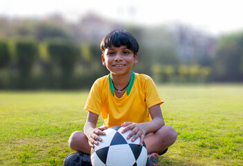 Wall Mural - Young boy sitting in the ground holding soccer ball	