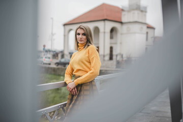 Sticker - Shallow focus shot of a Caucasian blonde leaning against a fence on a wooden bridge