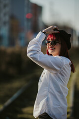 Poster - Vertical side view of a young smiling female with red hair, and a hat posing in a park