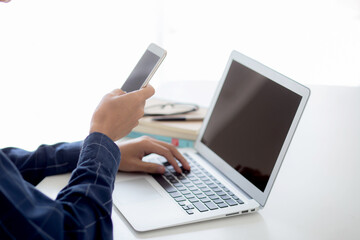Wall Mural - hand of young man working with laptop computer and smartphone mockup on desk at home, notebook and p