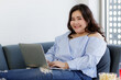 © Bangkok Click Studio - Asian young happy beautiful plus size sexy fat chubby smart female model sit relaxing on sofa smiling look at camera using laptop computer work from home in quarantine time from covid pandemic moment