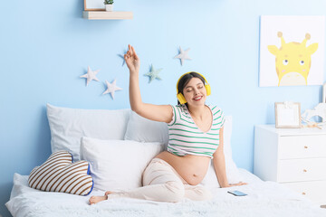 Wall Mural - Young pregnant woman listening to music at home