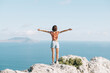 © Alex Photo - Rear view of brunette young woman standing with raised arms on the edge of a cliff  and enjoying of freedom on sunny day in summer vacations.