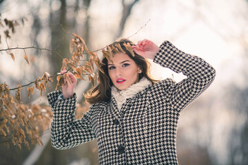 Canvas Print - Young brunette girl in a stylish winter outfit posing outside holding a dry tree branch