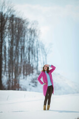 Poster - Brunette girl covering her face from the sun wearing a pink coat standing in the snow