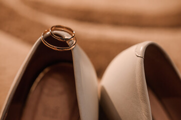 Wall Mural - White shoes of the bride and a pair of gold wedding rings on a brown background. Wedding accessories