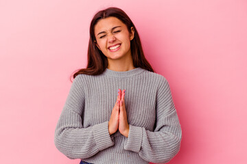 Young Indian woman isolated on pink background holding hands in pray near mouth, feels confident.