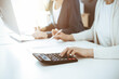 © Iryna - Accountant checking financial statement or counting by calculator income for tax form, hands closeup. Business woman sitting and working with colleague at the desk in office. Tax and Audit concept