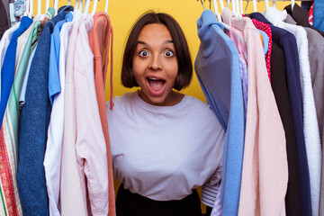 Young girl coming out of a coat rack isolated on yellow background