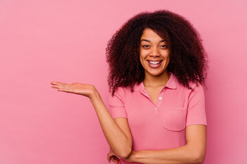 Wall Mural - Young african american woman isolated on pink background showing a copy space on a palm and holding another hand on waist.