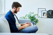 © baranq - Man at home sitting on sofa typing on laptop