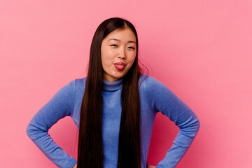 Young chinese woman isolated on pink background funny and friendly sticking out tongue.