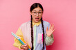 © Asier - Young chinese student woman holding books wearing a fashion multicolour shirt and braid, isolated on pink background receiving a pleasant surprise, excited and raising hands.