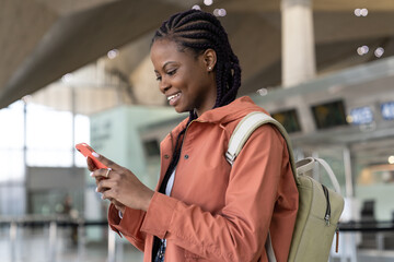 Happy black woman check message on smartphone after arrival of first flight after covid end in airport. Cheerful african female use mobile phone, traveler in terminal happy to travel in new normality