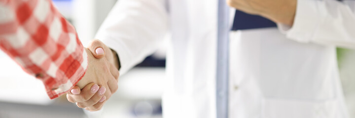 Wall Mural - Doctor holding clipboard and shaking hand of patient in clinic closeup