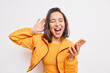 © WHstudio Leushin N - Overjoyed pretty Asian teenage girl got carried away with music holds smartphone enjoys favorite playlist via stereo headphones has relaxed carefree expression sings along wears orange jacket