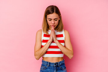 Wall Mural - Young caucasian woman isolated on pink background praying, showing devotion, religious person looking for divine inspiration.