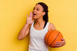 Young african american woman playing basketball isolated on yellow background shouting and holding palm near opened mouth.