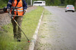 Closeup of a man with a lawn mower in his hands. A worker mows the grass on the side of the road. Improvement of the adjacent territory
